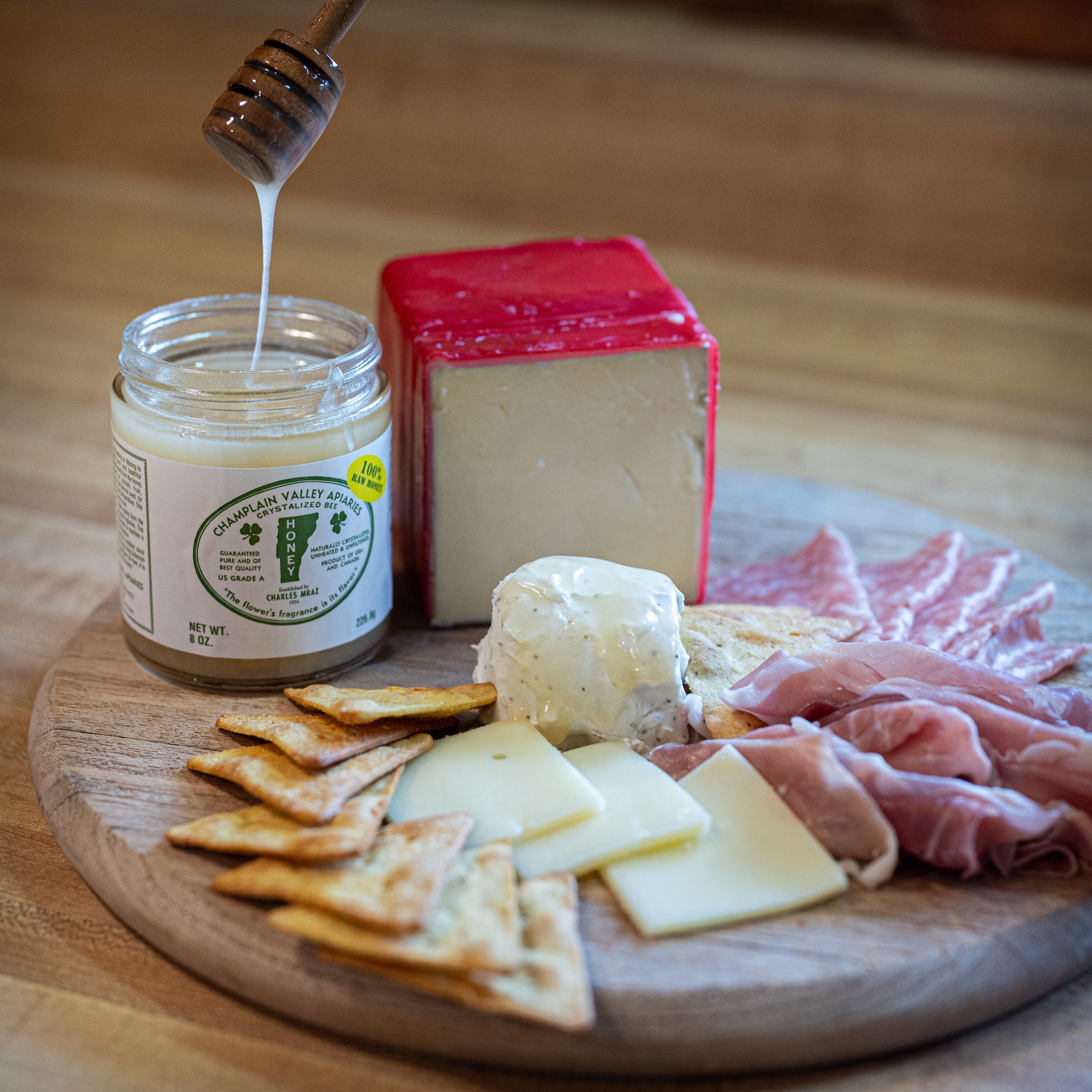 tableau of cheese, cracker and meat plate with a open jar of champlain valley apiaries raw honey